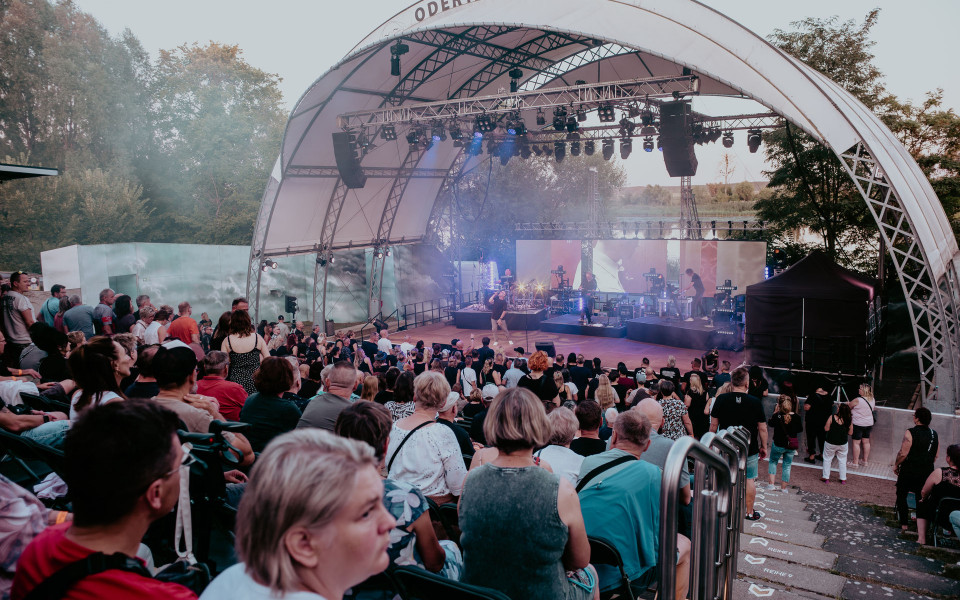 Auf der Odertalbühne findet ein Open-Air-Konzert vor einem gut besuchten Amphitheater statt. Die Bühne ist mit Lichtern, Lautsprechern und Nebel ausgestattet, während das Publikum auf den Rängen sitzt und steht.