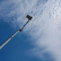Ein langer, weißer Arbeitsschein steht auf einem Teleskoparm in einem hellblauen Himmel mit flauschigen Wolken. Der Arbeitsschein ist von unten nach oben aufgenommen und dominiert den unteren Bildbereich.