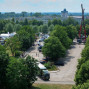 Das Foto zeigt eine Stadtlandschaft mit einem üppigen Park, der einen breiten Asphaltplatz überspannt. Im Hintergrund erheben sich Wohnhäuser und ein Hochhaus sowie eine Baustelle mit einem großen Krans.