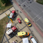Auf dem Foto ist eine belebte Straße mit mehreren Rettungswagen und einem Feuerwehrauto zu sehen, die sich in einem Vorfall befinden. Im Hintergrund ist ein grüner Rasen und ein Bürgersteig mit Fußgängern zu erkennen.