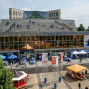 Das Foto zeigt das Herz- und Gefäßzentrum Schwedt mit einer beeindruckenden Treppenanlage und einer farbenfrohen Wandmalerei. Vor dem Gebäude befindet sich eine belebte Veranstaltung mit Besuchern, Ständen und Polizeiautos.
