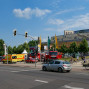Auf dem Foto ist eine Straße mit Gebäuden, darunter ein Großes Haus mit einer Bühne, beidseitig von Feuerwehrautos flankiert. Ein belebter Bürgersteig mit Fahrrädern und Fußgängern verläuft entlang der Straße.